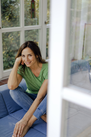 Lächelnde reife Frau sitzt auf der Couch zu Hause, lizenzfreies Stockfoto