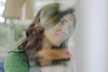Porträt einer lächelnden reifen Frau hinter einer Fensterscheibe - KNSF04727