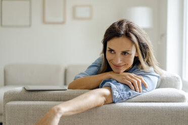 Porträt einer lächelnden reifen Frau, die sich zu Hause auf der Couch ausruht - KNSF04732