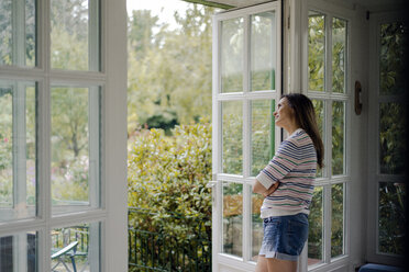Mature woman looking out of terrace door at home - KNSF04768