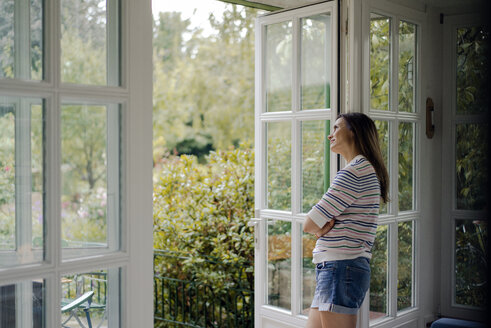 Reife Frau schaut aus der Terrassentür zu Hause - KNSF04768