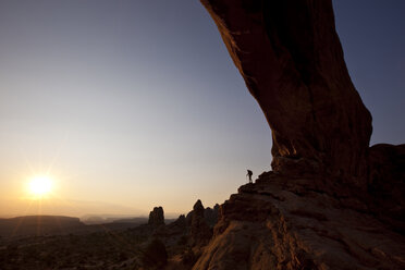 Ein Wanderer steht unter einem Bogen und betrachtet den Sonnenaufgang im Arches National Park, Utah. - AURF02599