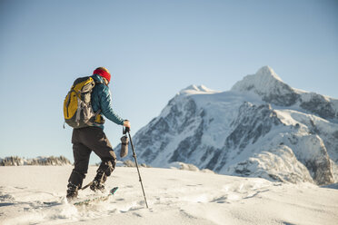 A female snowshoer crosses a snowfield with Mount Shuksan in the background. - AURF02633