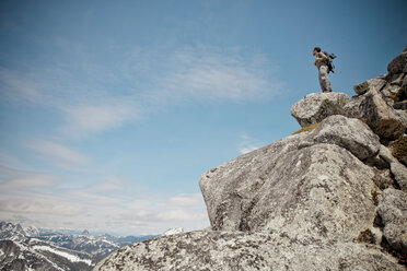A hiker stands on a pile of granite rock near the summit of Needle Peak. - AURF02637