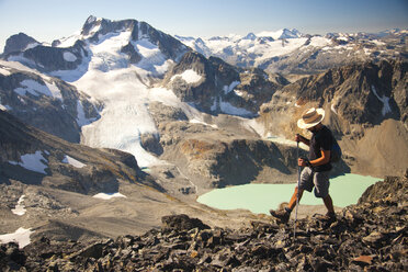 A hiker crosses a rocky ridge near Mount Cook with views of Wedge Mountain and Wedgemount Lake behind. - AURF02642