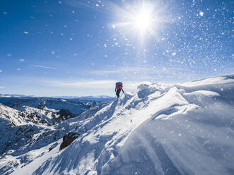 A hiker steps over a small cornice as snow swirls around them in White River National Forest, Colorado. - AURF02673
