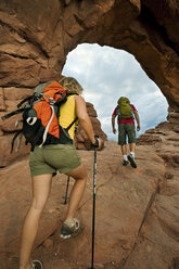 A man and woman hiking up to an arch in Arches National Park, Utah. - AURF02678
