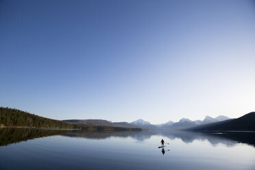 Ein Mann steht auf einem Stand Up Paddle Board (SUP) auf dem ruhigen Lake McDonald im Glacier National Park. - AURF02703