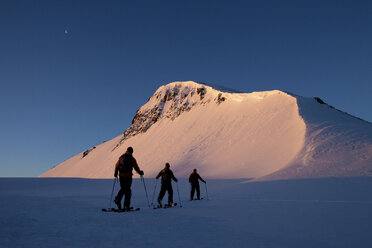 Drei Skitourengeher wandern im rosa Licht des Sonnenaufgangs auf einen Berg. - AURF02747