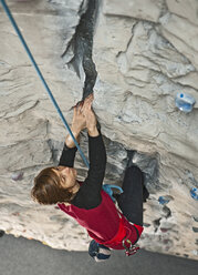 Frau klettert in einer Kletterhalle auf einen künstlichen Riss - AURF02826