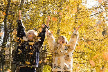 Zwei junge Mädchen (5 Jahre) spielen im Herbstlaub (werfen Blätter in die Luft), Fernie, British Columbia, Kanada. - AURF02842