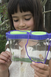 7-year-old girl holds a grasshopper in a container. - AURF02898