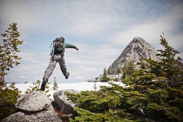 Ein Rucksacktourist springt kurz vor dem Gipfel des Needle PEak auf ein Stück Schnee. - AURF02920