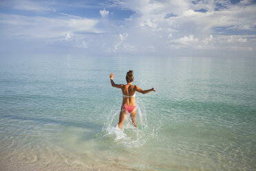 Eine junge Frau läuft während ihres Urlaubs in Kuba in seichtes türkisfarbenes Wasser. - AURF02975