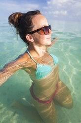 A young woman relaxes in shallow clear turquoise water . - AURF02976