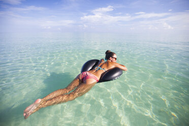 Eine junge Frau schwimmt auf einem aufblasbaren Wasserspielzeug im seichten türkisfarbenen Wasser. - AURF02977