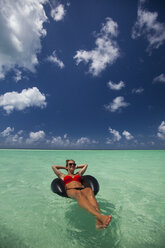 Eine junge Frau entspannt sich während ihres Urlaubs in Cayo Coco, Kuba, auf einem aufblasbaren Reifen im türkisfarbenen Wasser. - AURF02979