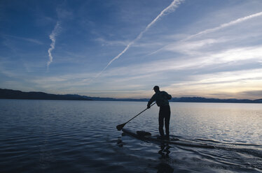 A young man stand-up paddleboards on a cold and clear winter day in Lake Tahoe, Nevada. - AURF02989