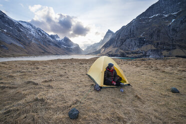 Weibliche Rucksacktouristin genießt die Aussicht vom Zelt beim Zelten am Strand von Horseid, Moskenes├©y, Lofoten, Norwegen - AURF03112