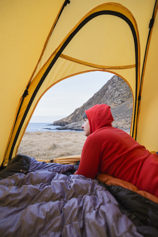 Weiblicher Rucksacktourist schaut aus dem Zelt beim wilden Zelten am Strand von Horseid, Moskenes├©y, Lofoten, Norwegen, lizenzfreies Stockfoto