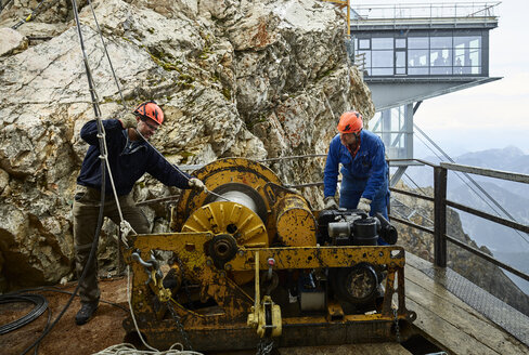 Deutschland, Bayern, Garmisch-Partenkirchen, Zugspitze, Monteure bei der Arbeit mit einer Seilrolle an einer Güterseilbahn - CVF01068