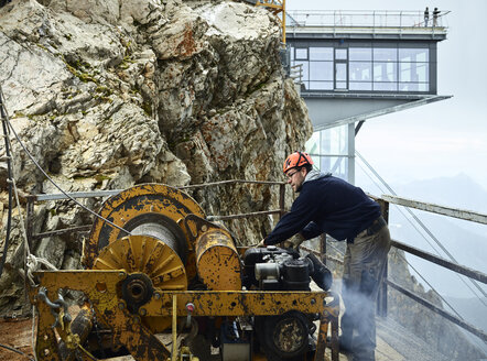 Deutschland, Bayern, Garmisch-Partenkirchen, Zugspitze, Monteur bei der Arbeit mit einer Seilrolle an einer Güterseilbahn - CVF01076