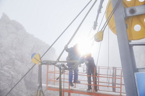 Deutschland, Bayern, Garmisch-Partenkirchen, Zugspitze, Monteure bei der Arbeit mit einer Seilrolle an einer Güterseilbahn - CVF01082