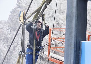 Germany, Bavaria, Garmisch-Partenkirchen, Zugspitze, installer working with rope pulley on goods cable lift - CVF01083