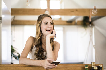 Happy brunette woman with cell phone at home - JOSF02539