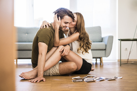 Glückliches, zärtliches Paar, das zu Hause sitzt und Fotos auf dem Boden macht, lizenzfreies Stockfoto