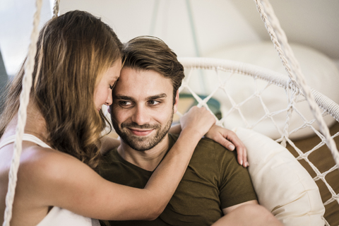 Glückliches, zärtliches Paar, das sich im Hängesessel zu Hause umarmt, lizenzfreies Stockfoto