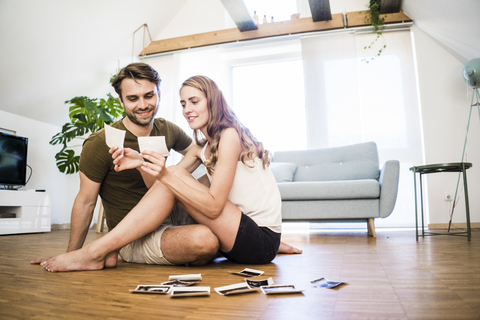 Happy couple sitting on the floor at home looking at ultrasound scans stock photo