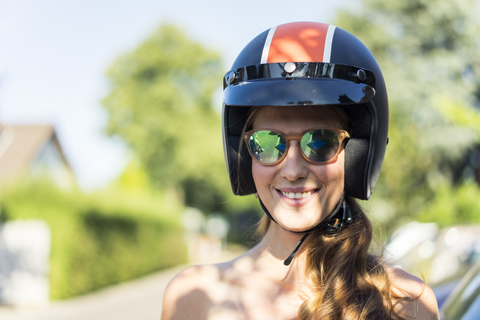 Porträt einer lächelnden Frau mit Sonnenbrille und Motorradhelm, lizenzfreies Stockfoto