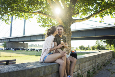 Happy couple sitting on a wall in summer eating ice cream - JOSF02613