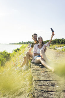 Glückliches Paar am Flussufer im Sommer, das ein Selfie macht - JOSF02616