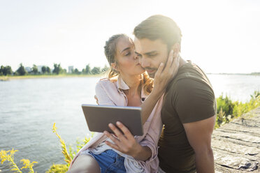 Couple kissing at the riverside in summer holding tablet - JOSF02618