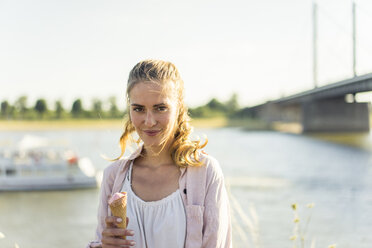 Porträt einer lächelnden Frau, die im Sommer am Flussufer ein Eis isst - JOSF02655