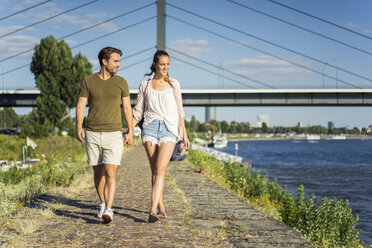 Glückliches Paar spaziert Hand in Hand auf der Uferpromenade im Sommer - JOSF02656