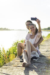 Glückliches Paar am Flussufer im Sommer, das ein Selfie macht - JOSF02662