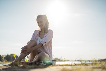 Porträt einer lächelnden Frau, die im Sommer am Flussufer sitzt - JOSF02667