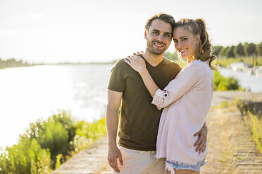 Portrait of smiling affectionate couple standing at the riverside in summer - JOSF02672