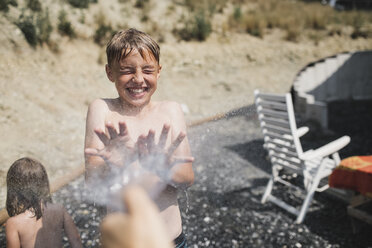 Porträt eines lachenden Jungen, der im Garten bespritzt wird - KMKF00447