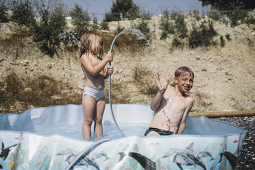 Brother and his little sister having fun together in pool in the garden - KMKF00448