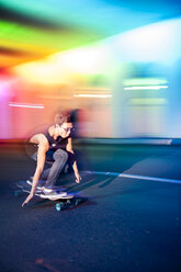 Young man skateboarding in colorfully lit traffic tunnel - AURF03276
