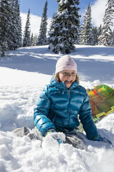 Young happy girl licking cold and snowy face after crashing while sledding on Molas Pass, Silverton, Colorado, USA - AURF03289