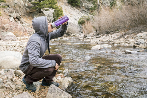 Junger Mann trinkt aus einer Wasserflasche am Fluss - AURF03292