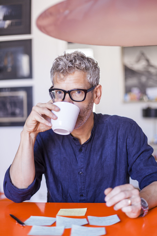 Porträt eines reifen Mannes am Tisch mit Notizblöcken, der Kaffee trinkt, lizenzfreies Stockfoto