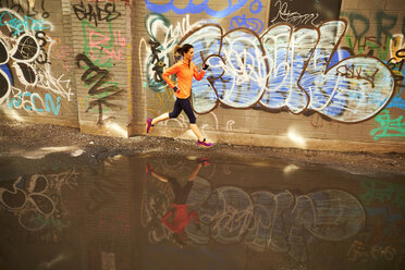 Frau läuft an einer Pfütze in einer mit Graffiti verzierten Gasse in Boston, Massachusetts, USA, vorbei - AURF03319