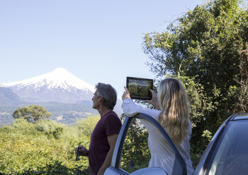 Frau fotografiert Vulkan mit Tablet vom Auto aus, Mann schaut zu - AURF03320