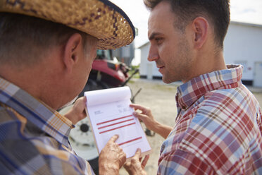 Two farmers analyzing data from clipboard on the farm - ABIF00941